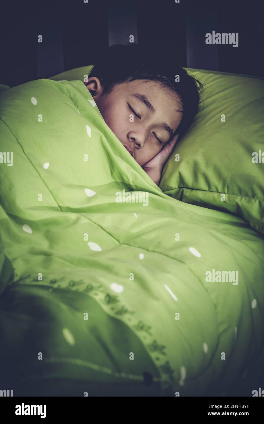 Concetto di bambino sano. Primo piano del bambino asiatico che dorme in pace. Il ragazzo carino dormite bene sul letto in camera di notte. Stile ad alto contrasto. Foto Stock