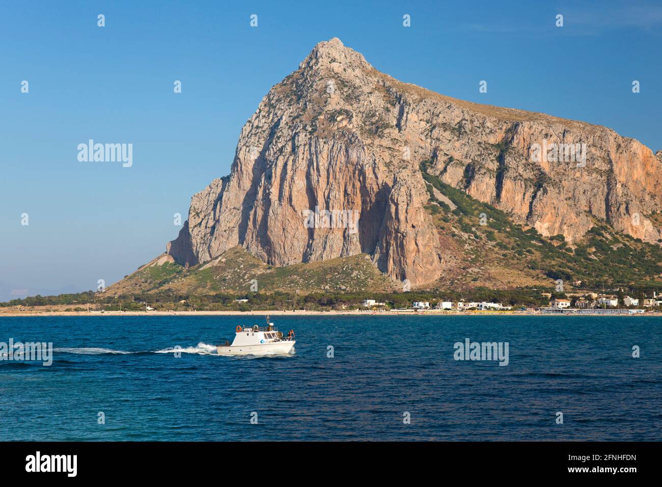 San Vito lo Capo, Trapani, Sicilia, Italia. Vista attraverso la baia fino all'imponente parete nord del Monte Monaco, piccola barca che ritorna al porto. Foto Stock