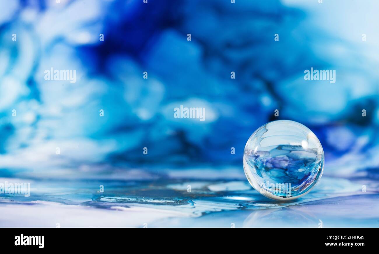 Una palla di vetro trasparente su uno sfondo astratto blu. La tecnica dell'inchiostro alcolico. Spazio di copia. Foto Stock