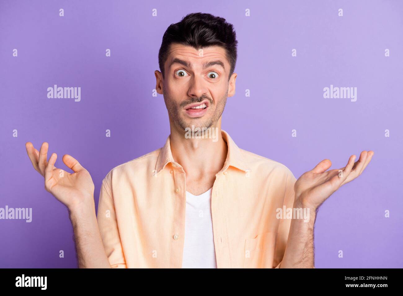 Foto di fastidioso ragazzo pazzo sollevare palme grimacing fissando l'usura camicia beige isolato colore viola sfondo Foto Stock