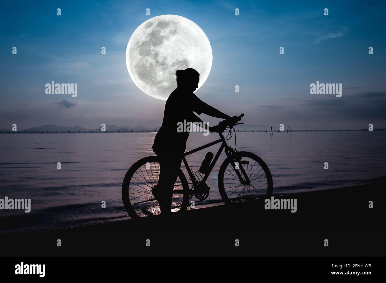 Silhouette di ciclisti in azione godendo la vista sul mare su luminoso sfondo cielo di luna piena. Stile di vita attivo all'aperto per un concetto sano. Il Foto Stock