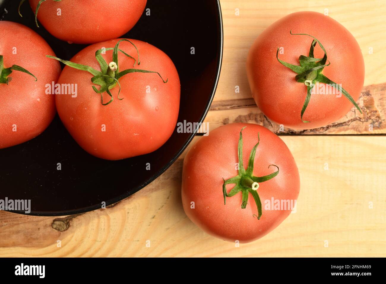 Diversi pomodori rosa maturi in un piatto di ceramica nera, primo piano, su un tavolo di legno, vista dall'alto. Foto Stock