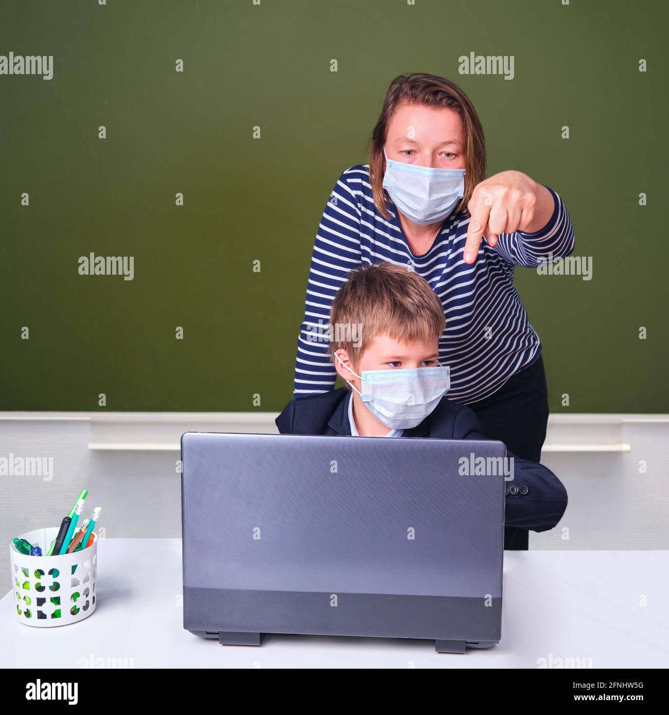 Insegnante e scolaro durante l'apprendimento a distanza nella scuola elementare, concetto di problemi su sfondo lavagna Foto Stock