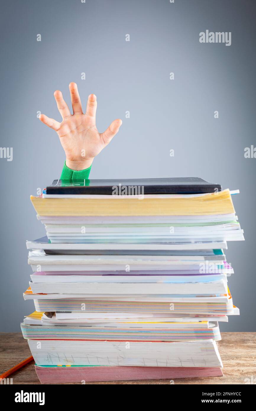 Immagine concettuale astratta che mostra a un giovane studente dietro una grande pila di libri di preparazione dei test su un banco di studio. Un carico eccessivo. Il capretto sta provando a rais Foto Stock