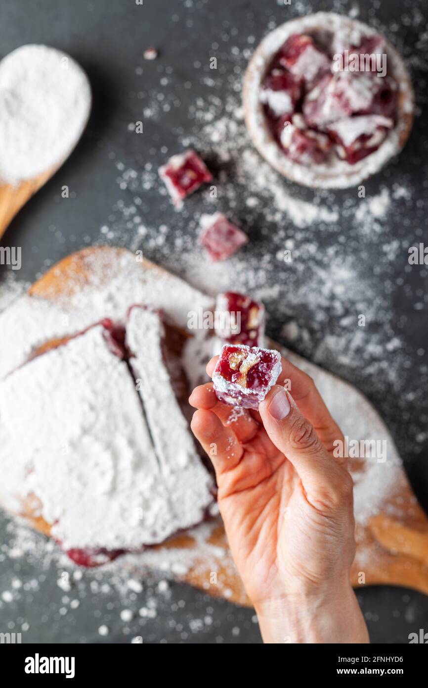 Una donna sta tenendo un pezzo a forma di dadi di frutta e frutta aromatizzata in casa delizia turca ricoperta di zucchero di pasticceria in polvere. In background in Foto Stock