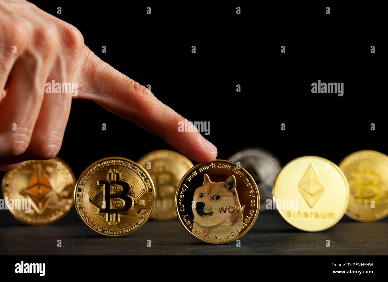 I tipi simbolici di criptovaluta rappresentati come monete lucide sono allineati su sfondo scuro. Tra loro il dogecoin che ha cominciato come scherzo è currentl Foto Stock