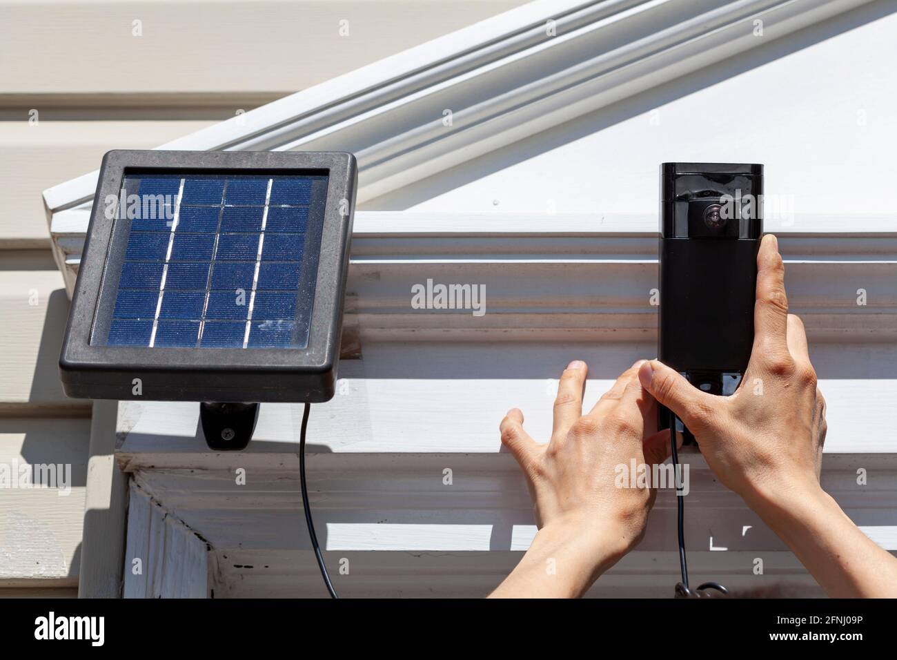 Una donna caucasica sta installando una telecamera wireless di sorveglianza con sensore di movimento sulla parte superiore del telaio della porta anteriore. La telecamera è collegata a a. Foto Stock