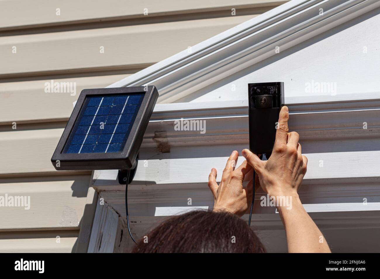Una donna caucasica sta installando una telecamera wireless di sorveglianza con sensore di movimento sulla parte superiore del telaio della porta anteriore. La telecamera è collegata a a. Foto Stock