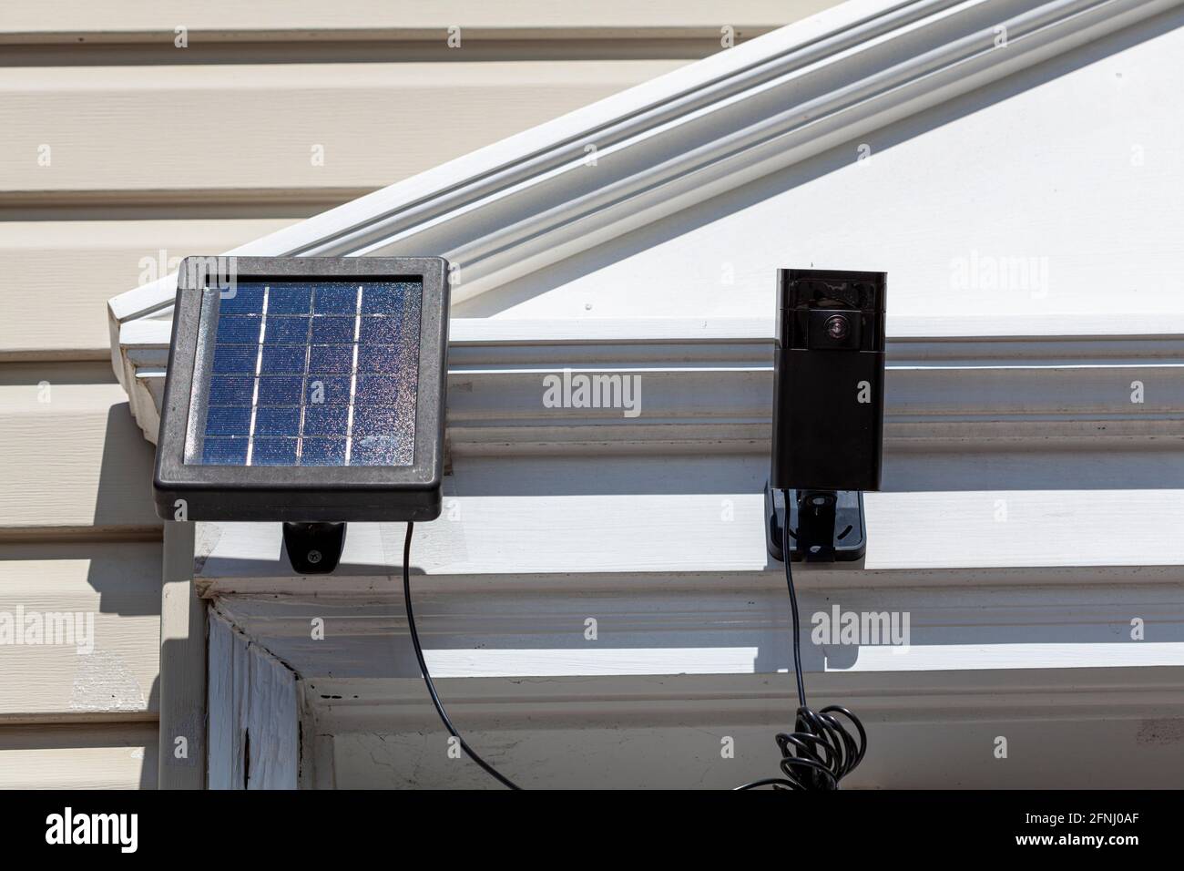 una telecamera wireless di sorveglianza con sensore di movimento sulla parte superiore del telaio dello sportello anteriore. La telecamera è collegata a un pannello solare per venerdì ambientale Foto Stock