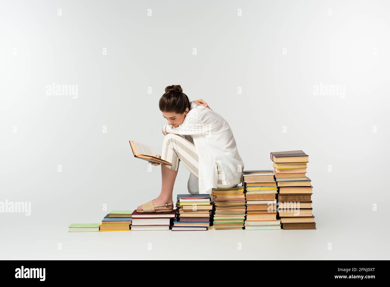 tutta la lunghezza di giovane donna che gratta indietro mentre si siede sopra pila di libri su bianco Foto Stock