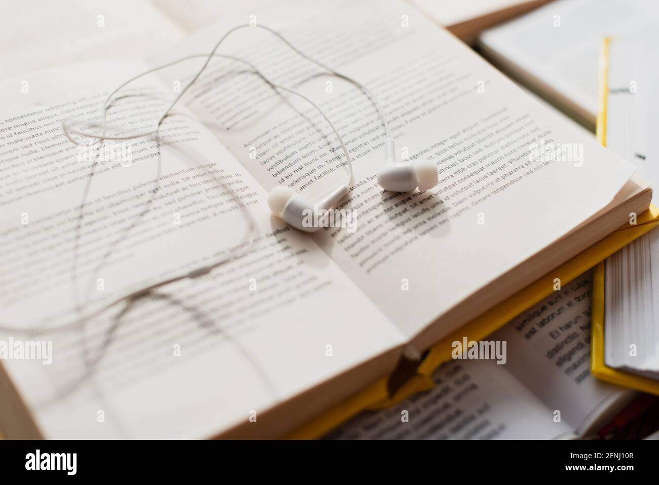 auricolari bianchi su una pila di libri sfocati Foto Stock