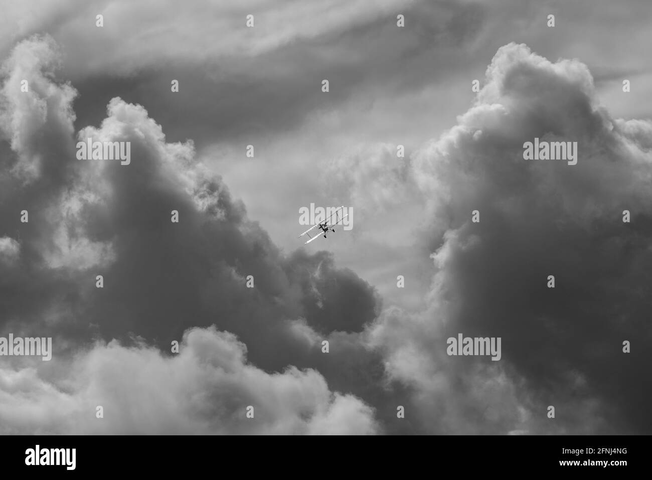 Incredibile immagine mono come un piccolo biplano sale verso torreggiante nuvole con luce solare che si stendono dalle ali inclinate Foto Stock