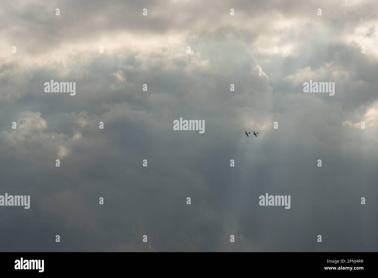 Immagine a colori di due velivoli Spitfire in formazione alta in il cielo e tenuto in un fascio di luce solare contro nuvole molto più scure Foto Stock