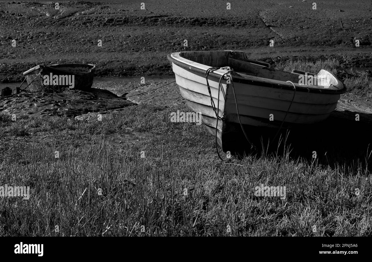 Immagine mono di due piccole barche a remi catturate in anticipo luce solare serale legata e pronta per l'uso da un entrata corrente Foto Stock