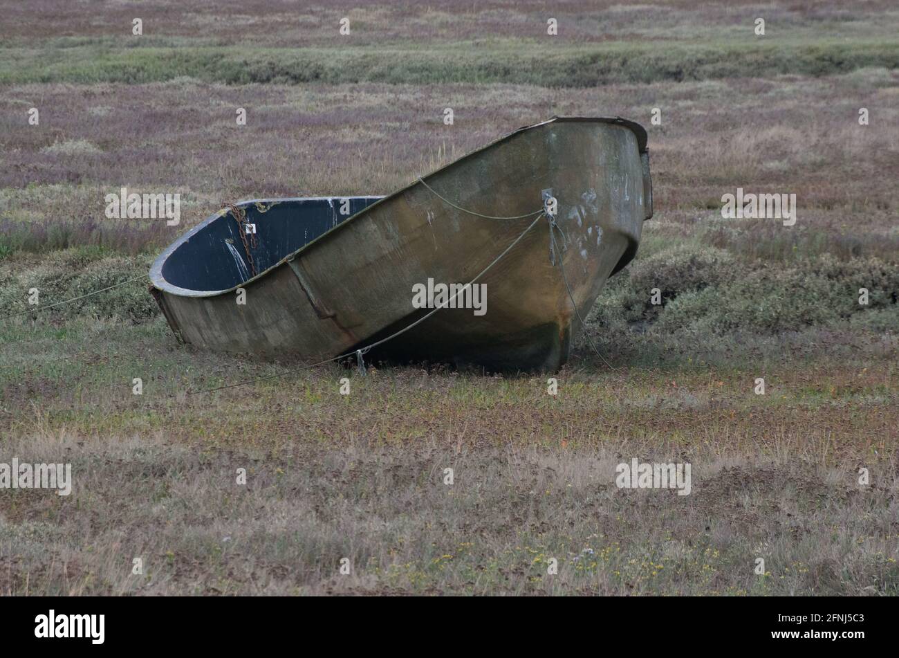 Imbarcazione a remi in metallo singola e piccola legata tra la vegetazione Da un'insenatura del mare sulla costa nord del Norfolk Foto Stock