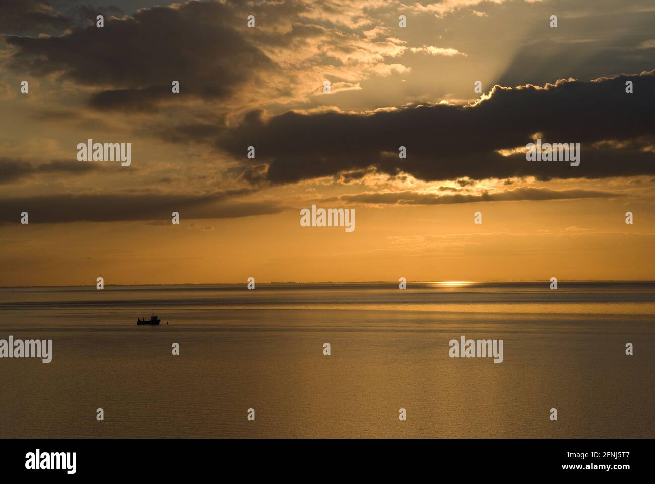 Un'immagine di un tramonto perfetto lungo la costa di Norfolk con il bagliore dorato della prima sera e una barca da pesca in silhouette su un mare tranquillo e tranquillo Foto Stock