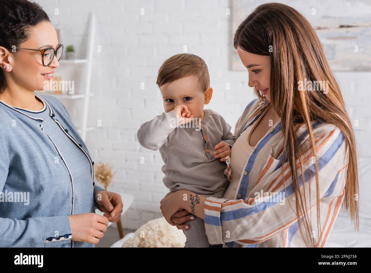 madre sorridente che tiene in armi bambino ragazzo vicino afroamericano amico in occhiali Foto Stock