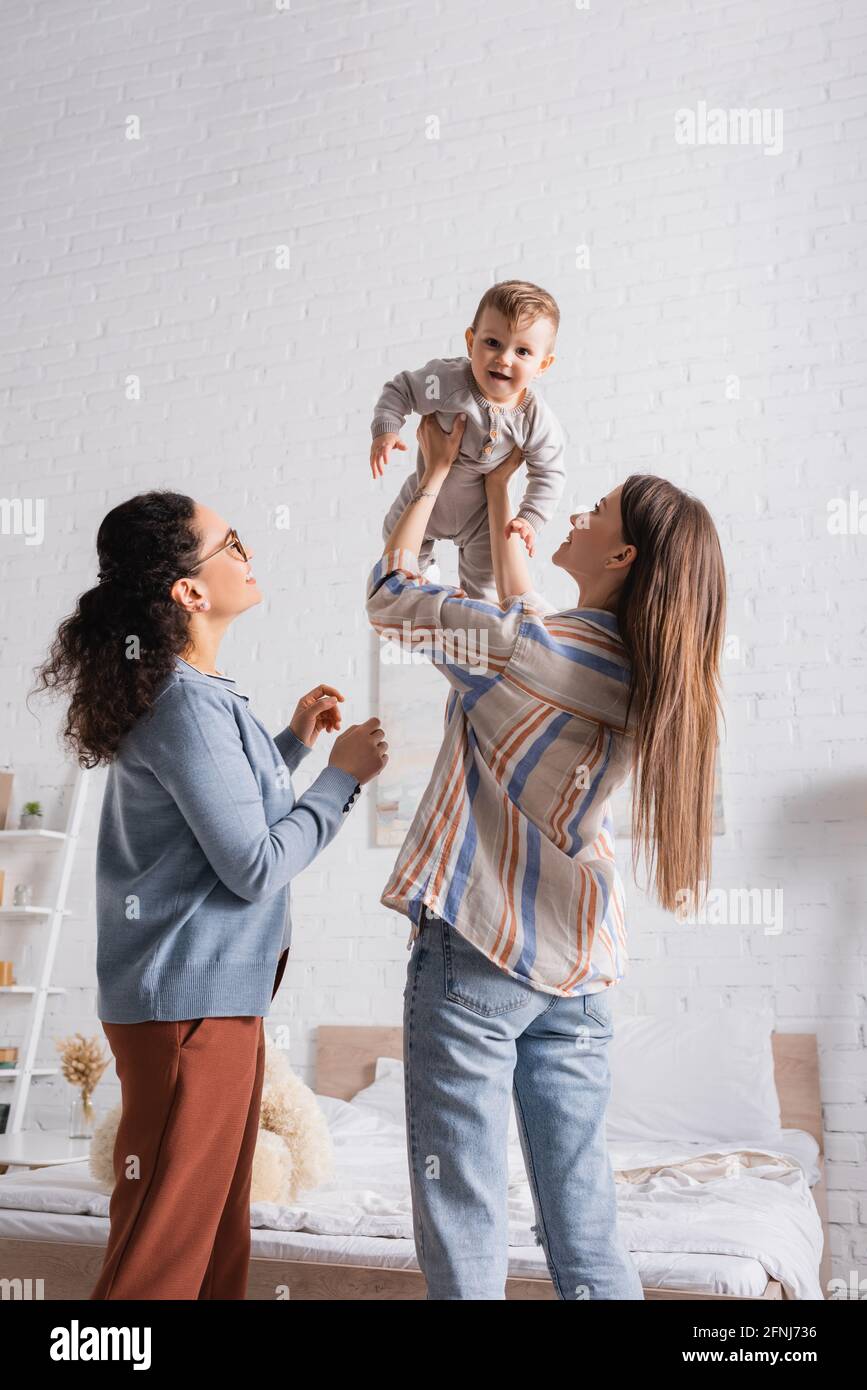 madre positiva che tiene in armi bambino ragazzo vicino afroamericano amico Foto Stock