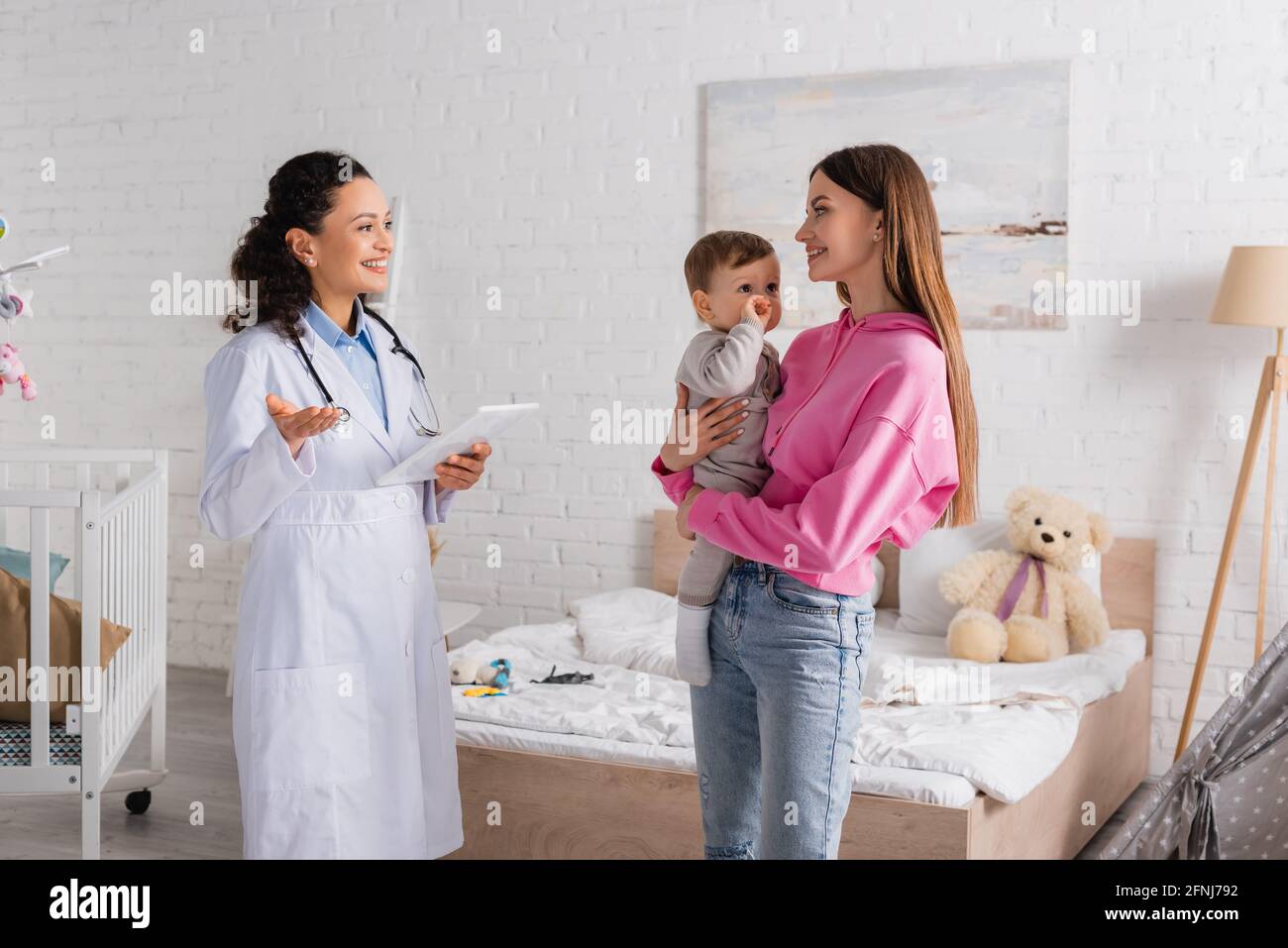 felice madre che tiene in armi bambino ragazzo vicino afroamericano pediatra con tablet digitale Foto Stock