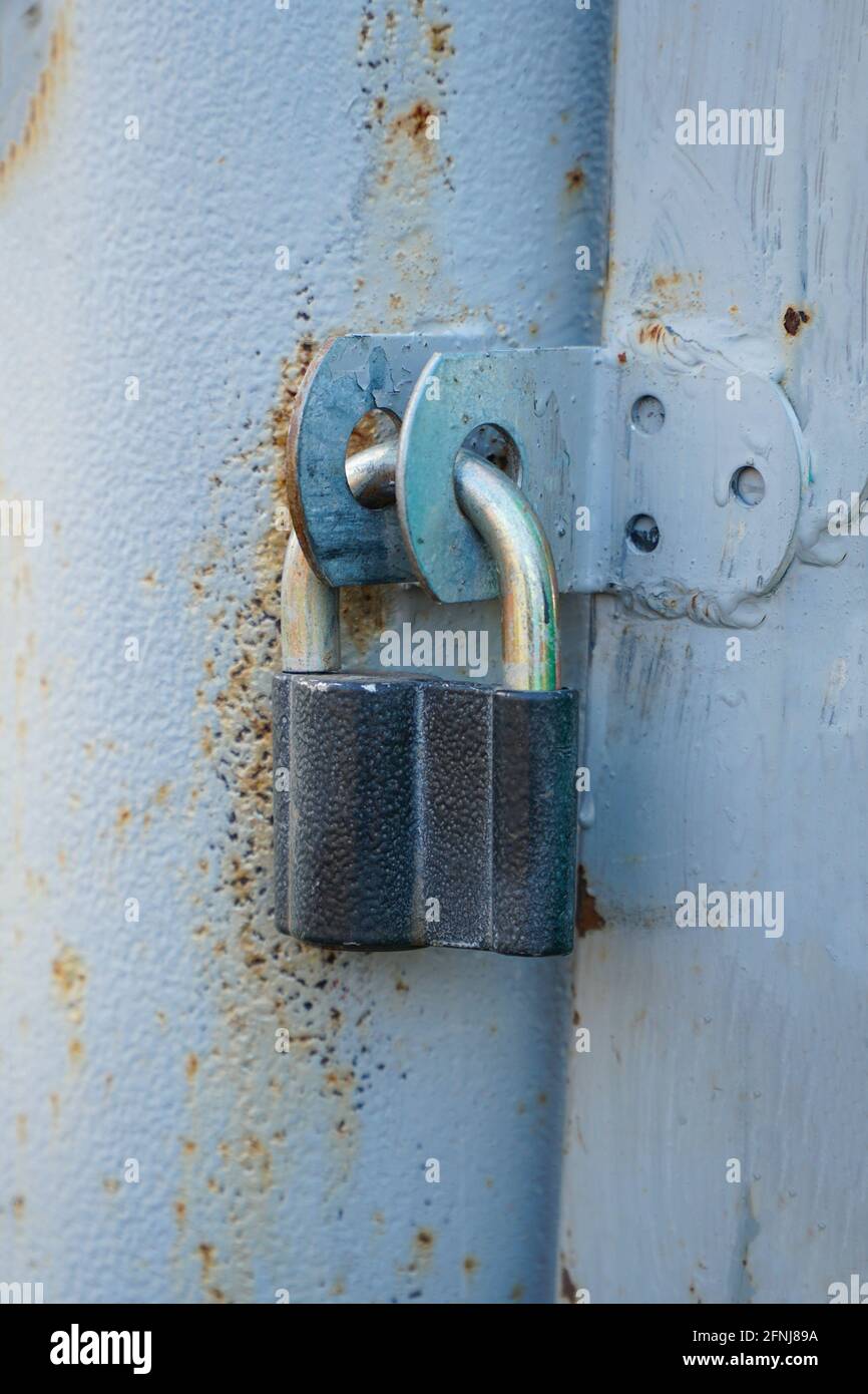 Lucchetto chiuso appeso alle cerniere del ferro grigio porta Foto Stock