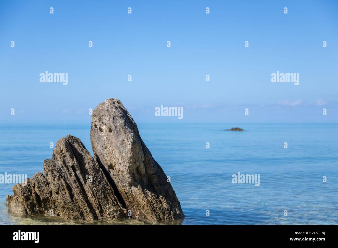 Oceanscape, una grande roccia siede al bordo dell'acqua, l'acqua blu e il cielo blu Foto Stock