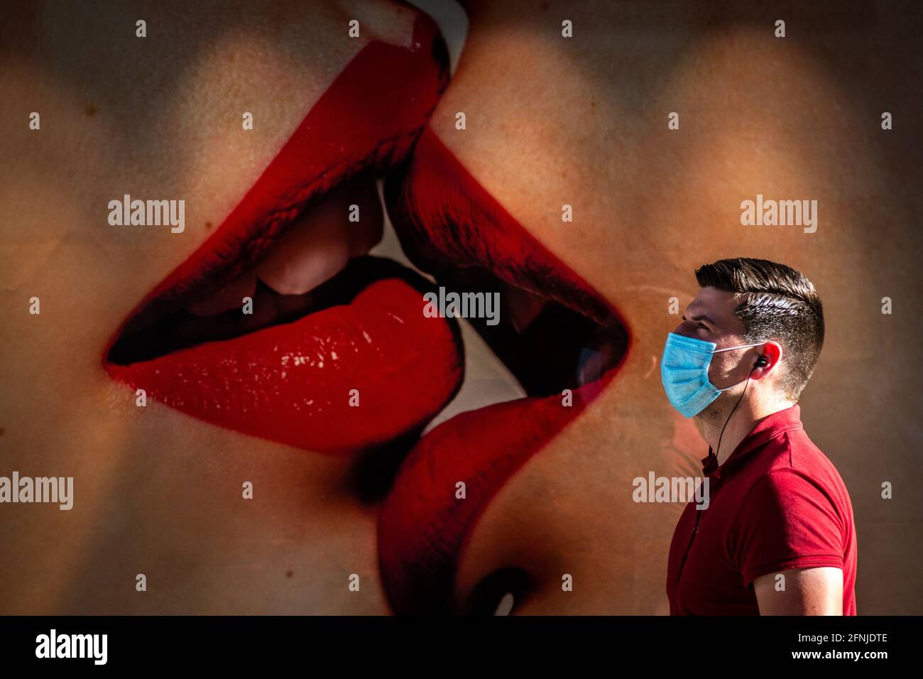 Madrid, Spagna. 17 maggio 2021. Un uomo che indossa una maschera facciale per fermare la diffusione del coronavirus (COVID-19) passa davanti a un annuncio pubblicitario con l'immagine di due donne che baciano. Fernando Simon, direttore del Centro di coordinamento per gli allarmi sanitari e le emergenze del Ministero della Salute, ha dichiarato oggi in una conferenza stampa 'abbiamo già 7.2 milioni di persone vaccinate con il calendario completo e almeno 15 milioni con almeno una dose. È molto probabile che all'aperto, in pochi giorni, l'uso della maschera facciale possa essere ridotto. Credit: Marcos del Mazo/Alamy Live News Foto Stock