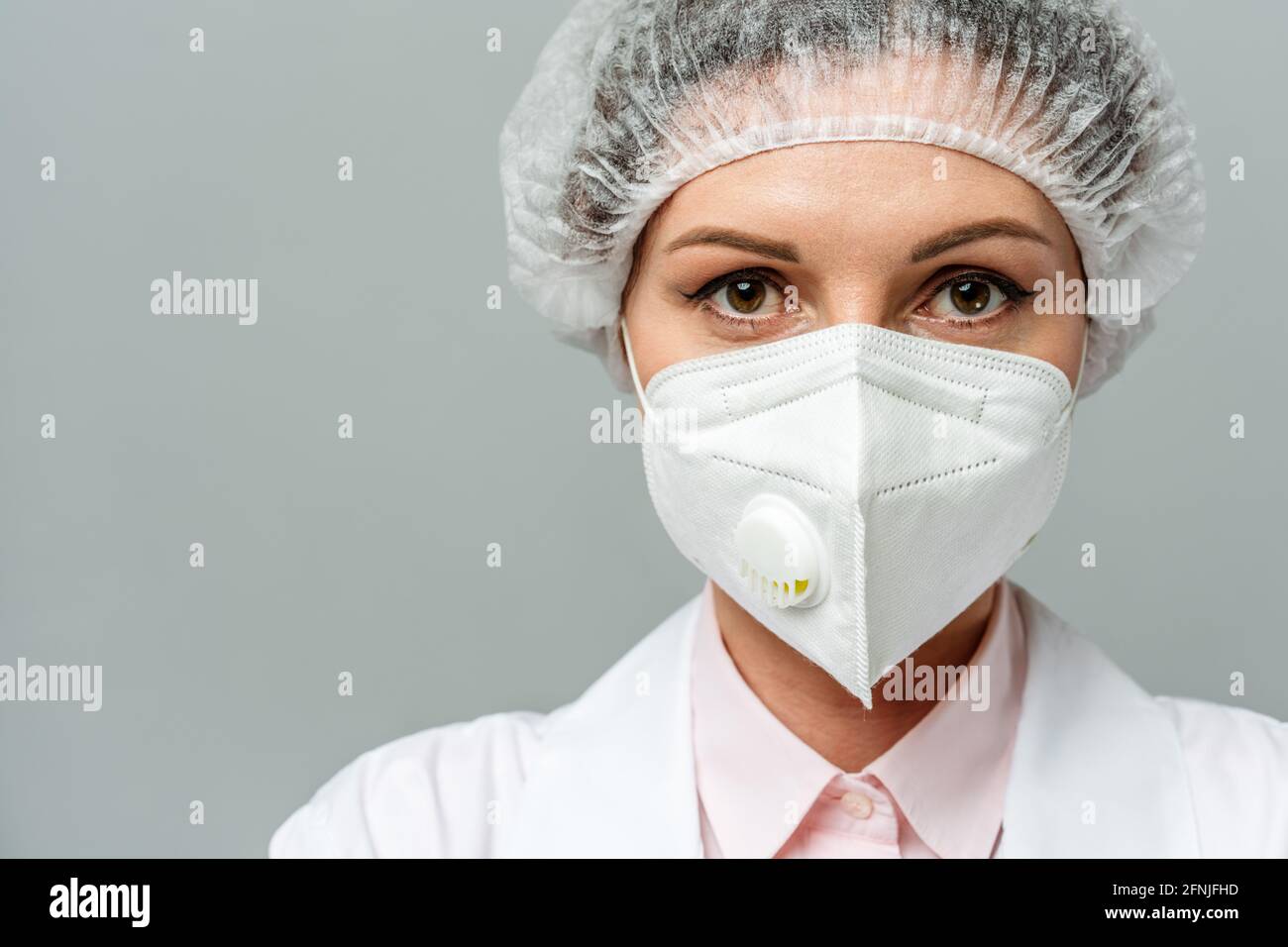 Ritratto di una giovane donna infelice medico in una maschera medica su sfondo grigio. Gli occhi stanchi del medico. Il concetto di coronavirus. Foto Stock