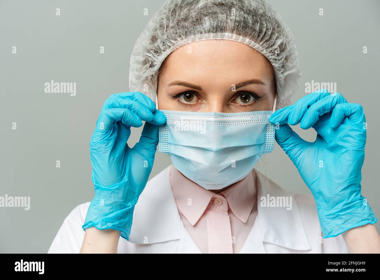 Ritratto di una giovane donna infelice medico in una maschera medica su sfondo grigio. Gli occhi stanchi del medico. Il concetto di coronavirus. Foto Stock