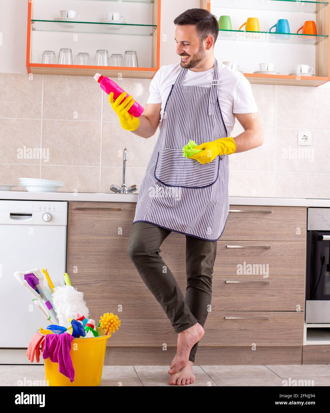Bell'uomo giovane con grembiule e guanti che tengono prodotti per la  pulizia davanti agli armadi da cucina Foto stock - Alamy