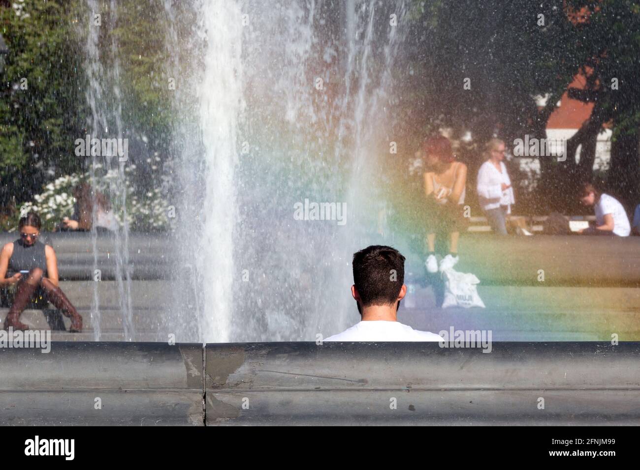 Giovane uomo che riposa vicino alla fontana con arcobaleno sullo sfondo al Washington Square Park a New York, Stati Uniti Foto Stock