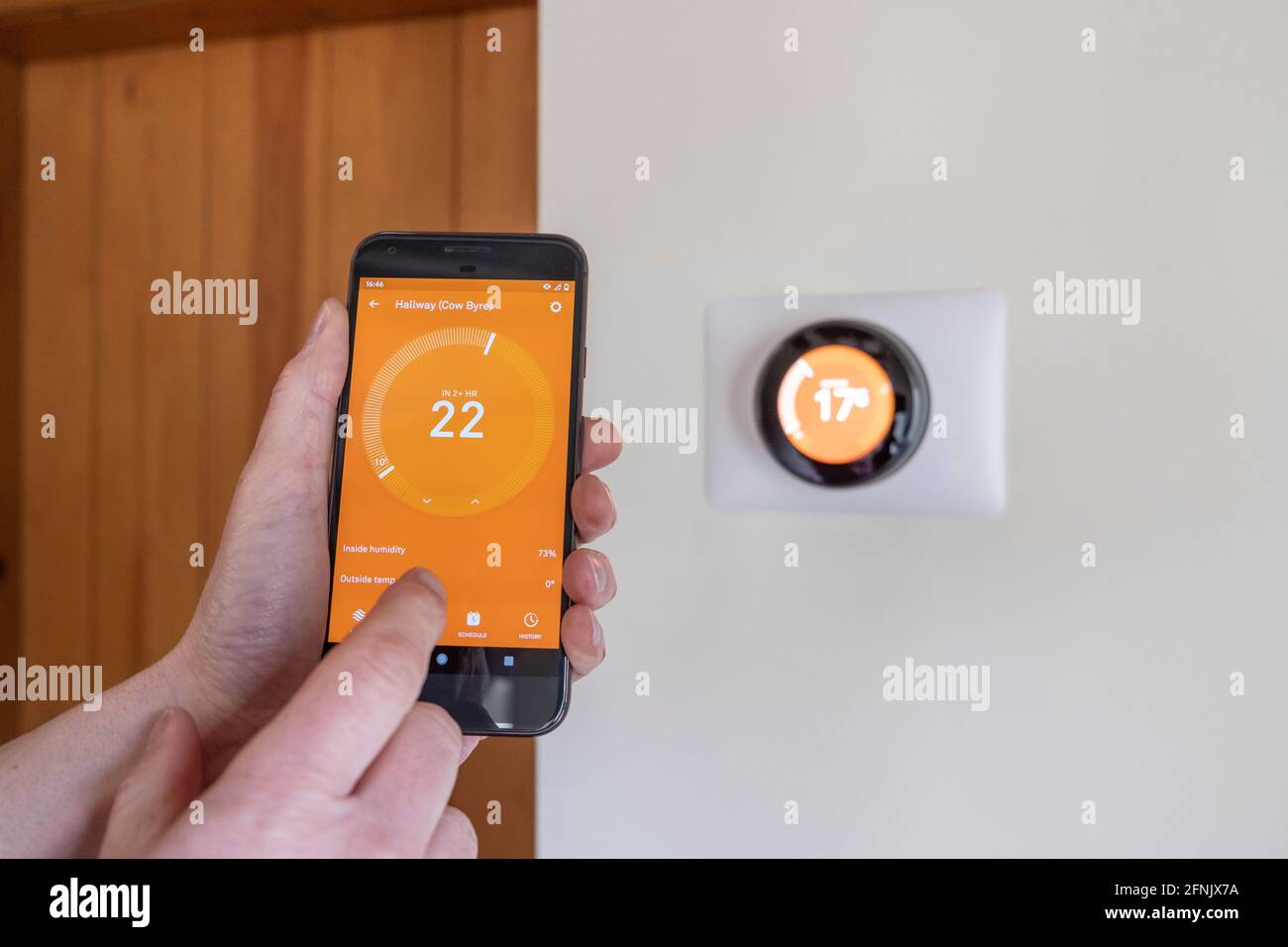 Persona che controlla la temperatura su un termostato intelligente tramite un'app di un telefono Foto Stock