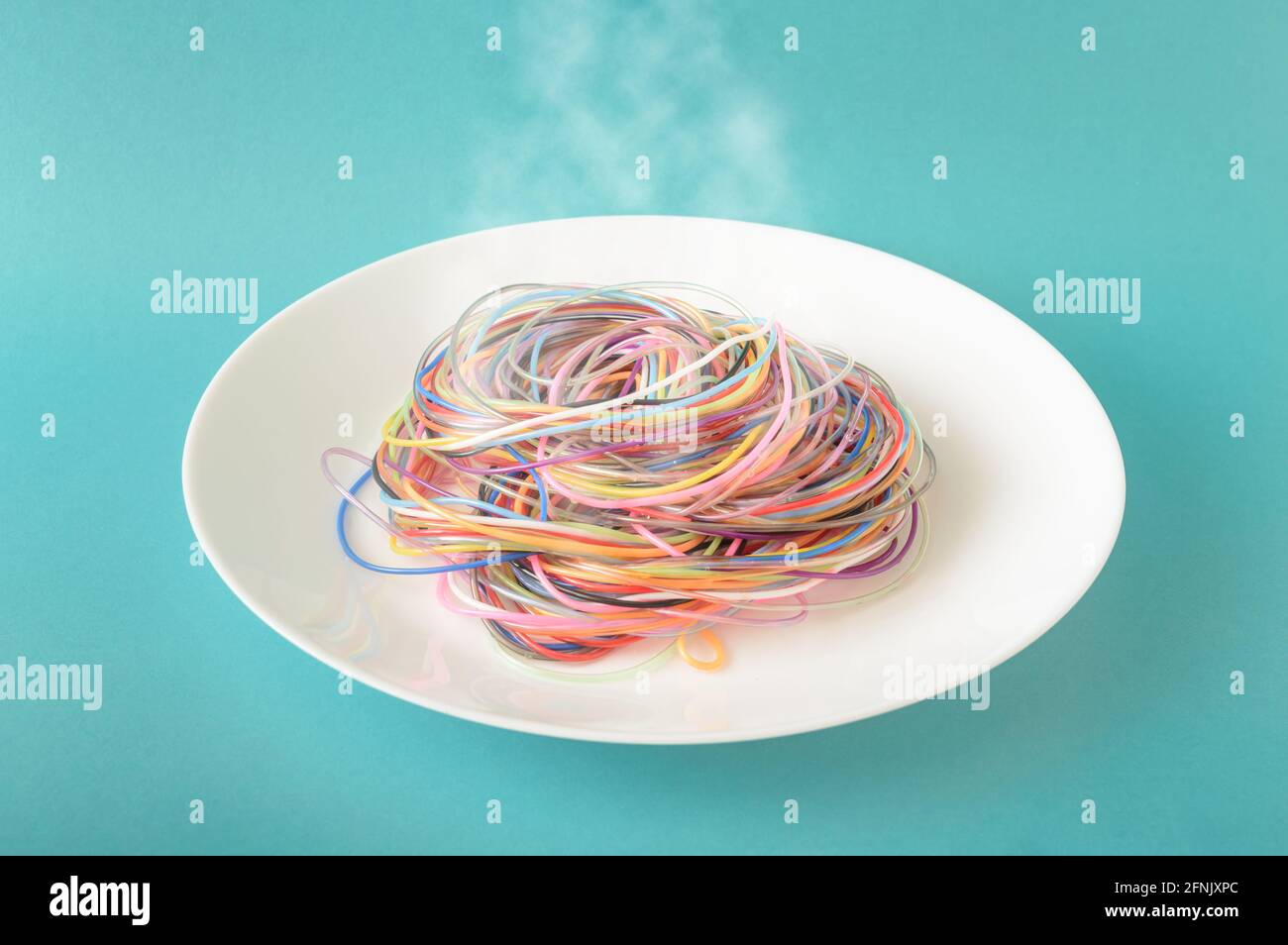 Cavi colorati su una piastra da cui fuoriesce vapore su sfondo blu. Un concetto ispirato agli spaghetti e al cibo. Stile fotografico minimo. Foto Stock
