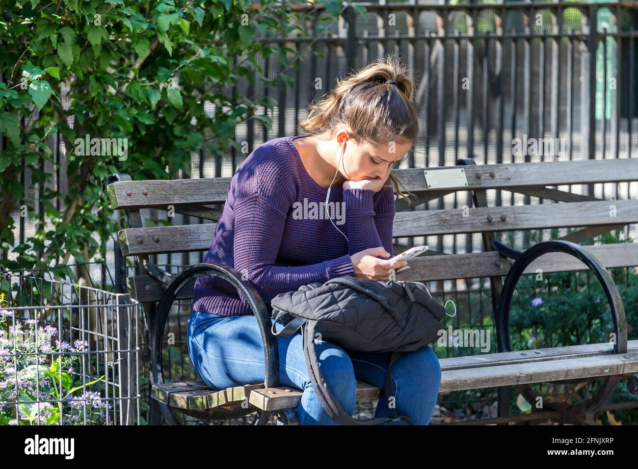 Giovane donna caucasica che controlla i social media attraverso il suo cellulare al parco di New York, USA Foto Stock
