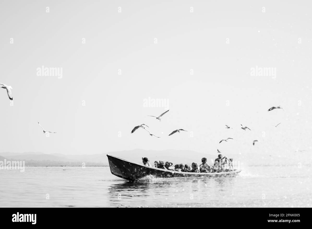 Inle Lake, Nyaung Shwe, Shan state, Myanmar - 7 gennaio 2020: La gente del posto viaggia in barca tradizionale con uccelli sopra e montagne sullo sfondo Foto Stock