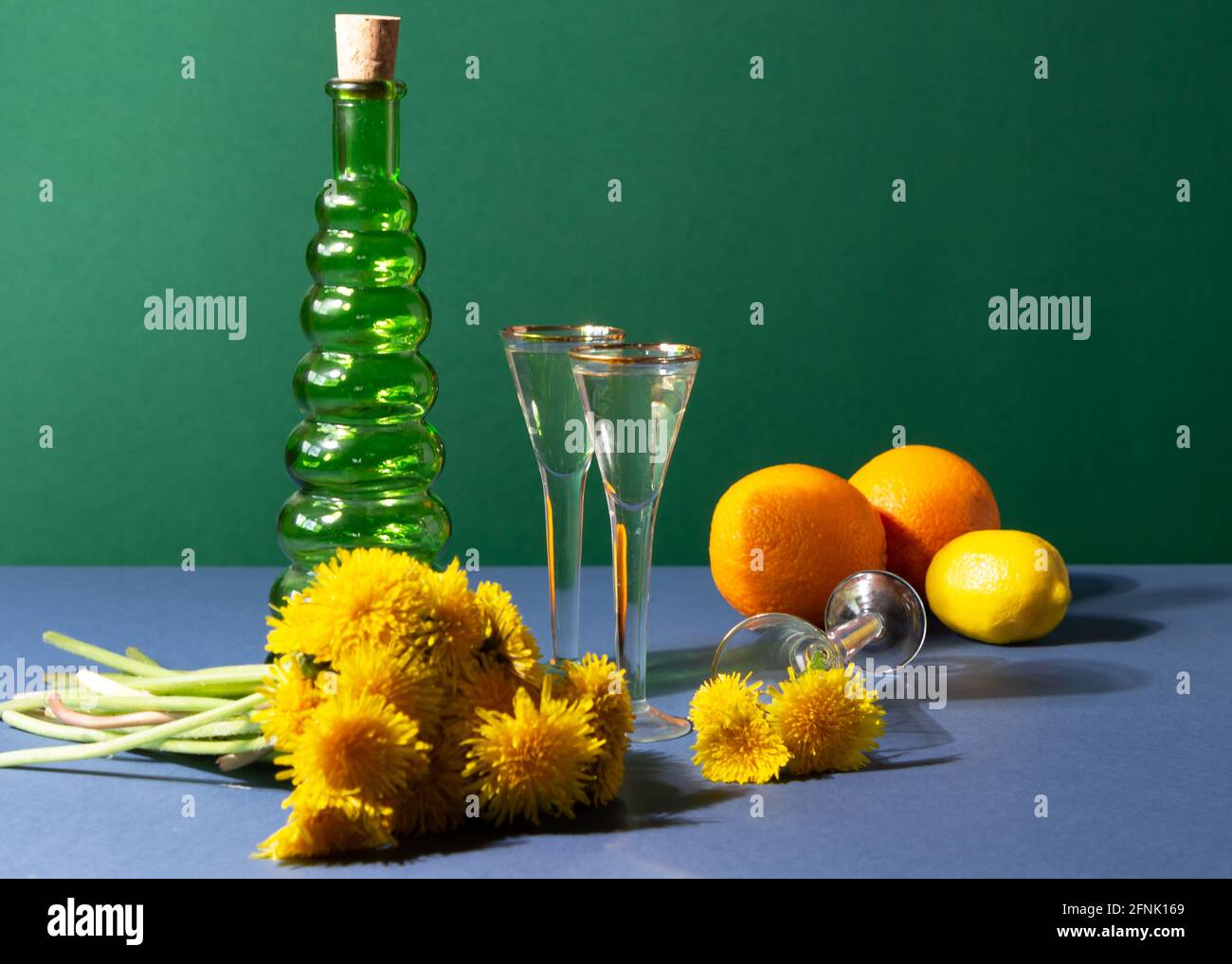 Dente di leone vino in verricelli d'annata. Moderna natura morta con ingredienti per la preparazione di miscele di erbe. Bottiglia verde, due arance, lime e bouquet Foto Stock