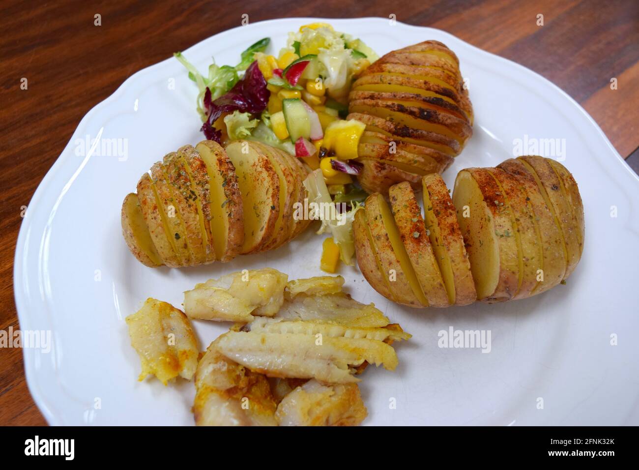 Pranzo con patate al forno, insalata e pesce fritto su piatto bianco, pronto a mangiare. Foto Stock