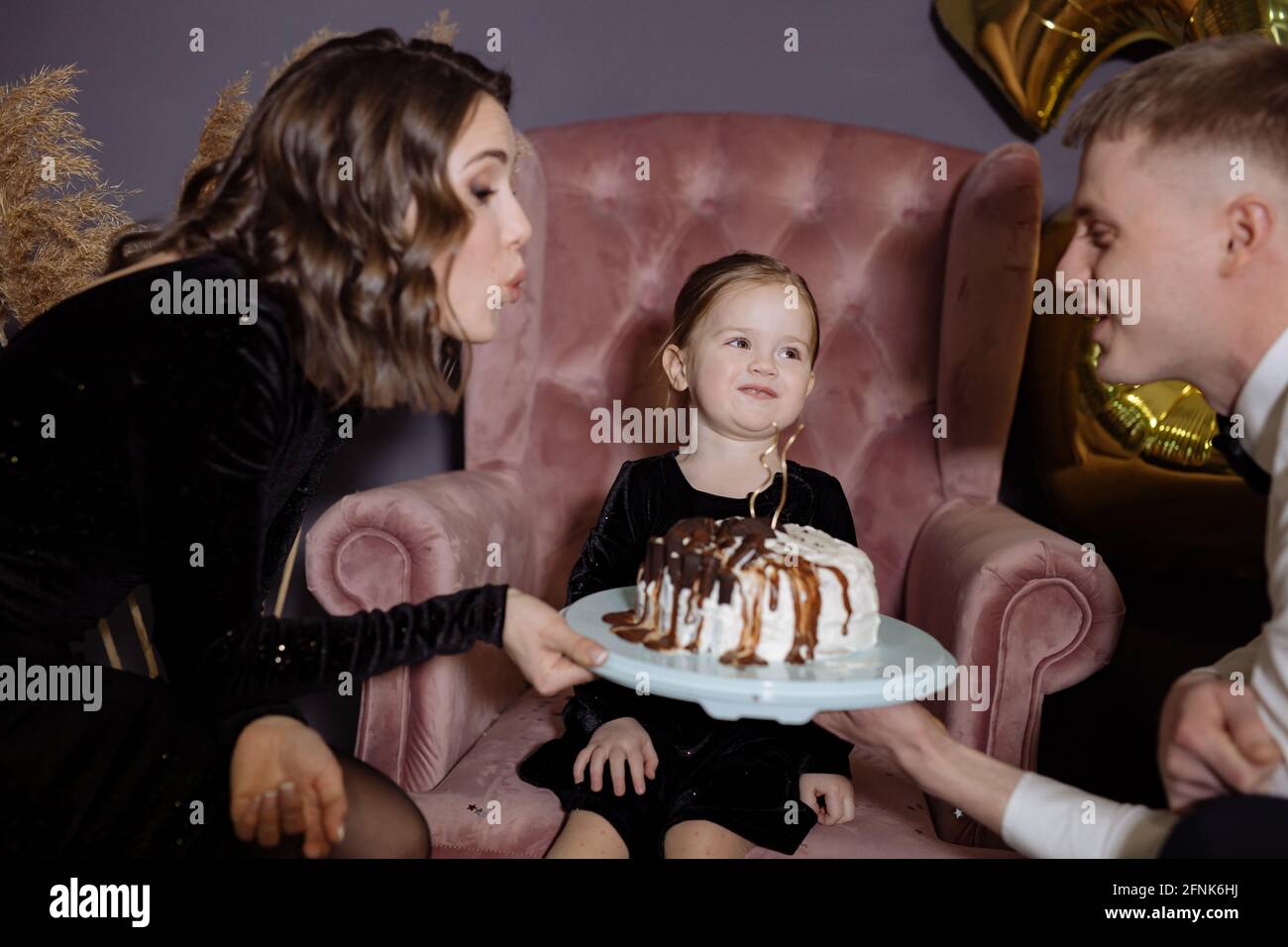 La bambina soffia fuori le candele sulla torta con i suoi genitori Foto Stock