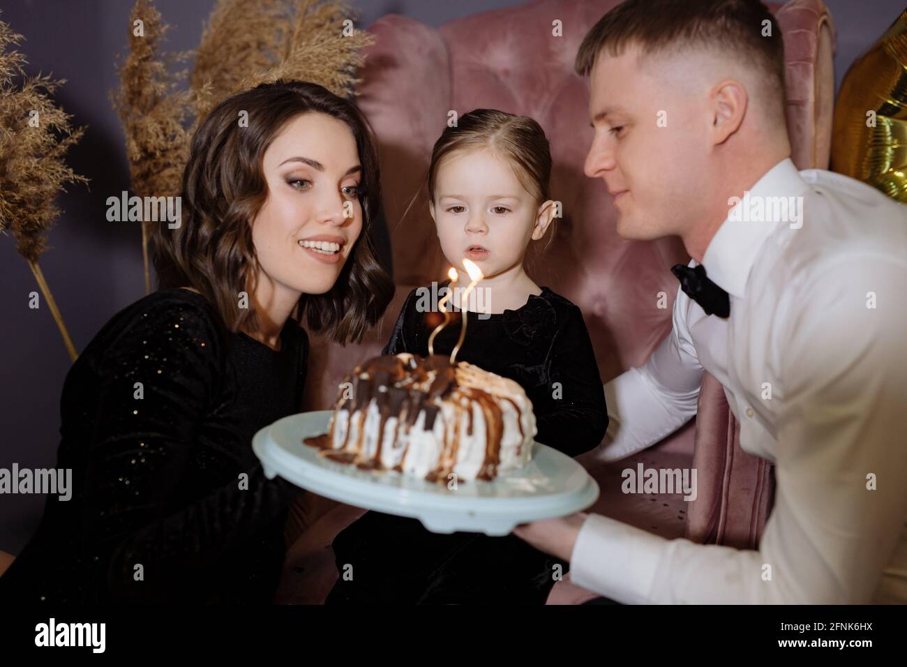 La bambina soffia fuori le candele sulla torta con i suoi genitori Foto Stock