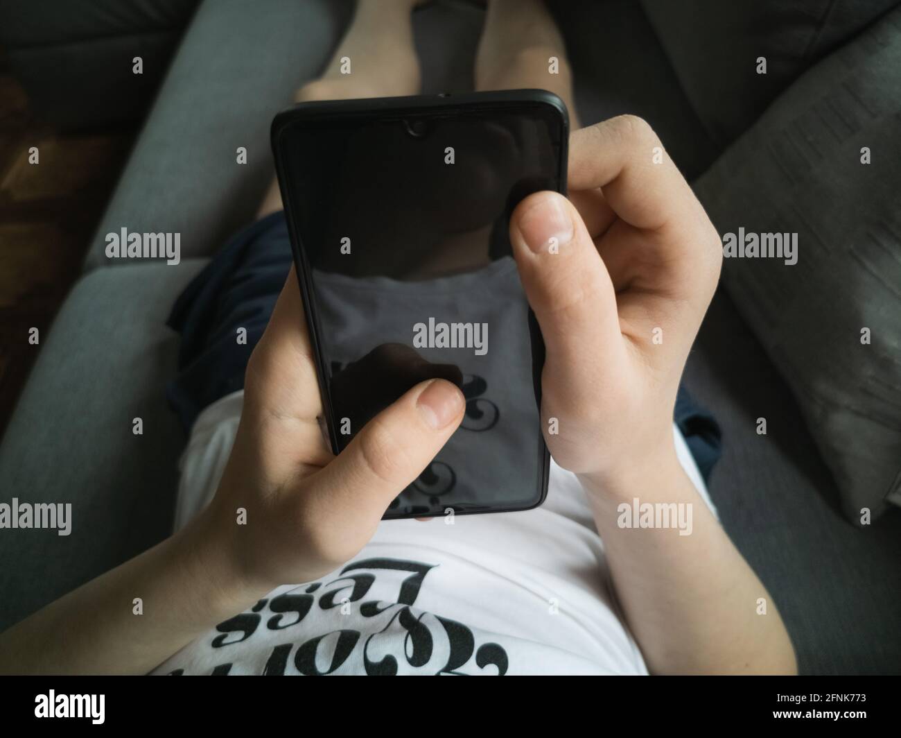 Ragazzo di 13-15 anni sul divano con uno smartphone nelle sue mani Foto Stock