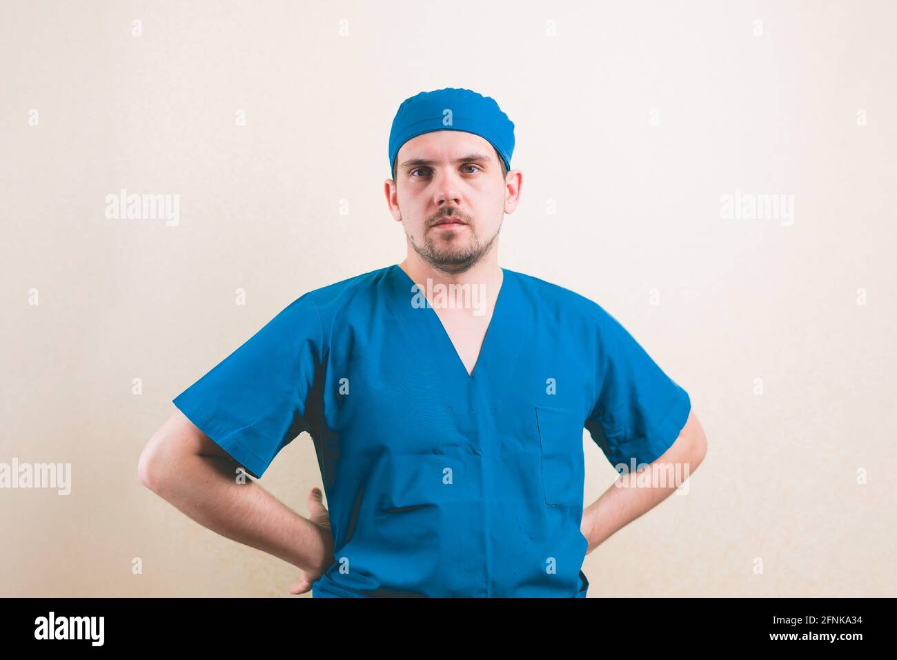 Giovane ritratto medico con le mani sui fianchi in chirurgo blu tuta e maschera respiratoria protettiva su sfondo giallo isolato Foto Stock