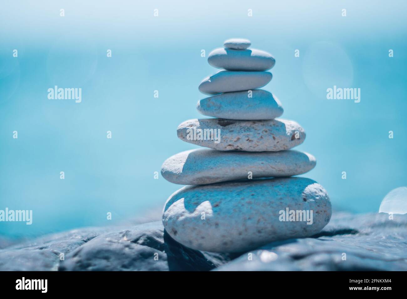 Equilibrata piramide di ciottoli sulla spiaggia in una giornata di sole. Abstract Sea bokeh sullo sfondo. Messa a fuoco selettiva. Pietre Zen sulla spiaggia di mare, meditazione Foto Stock
