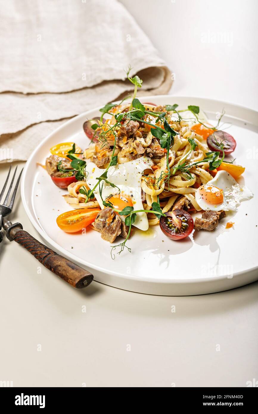 Primo piano di deliziosi spaghetti fatti in casa con verdure, formaggio e uova di quaglia fritte su un piatto rotondo su uno sfondo chiaro. Cucina tradizionale italiana Foto Stock