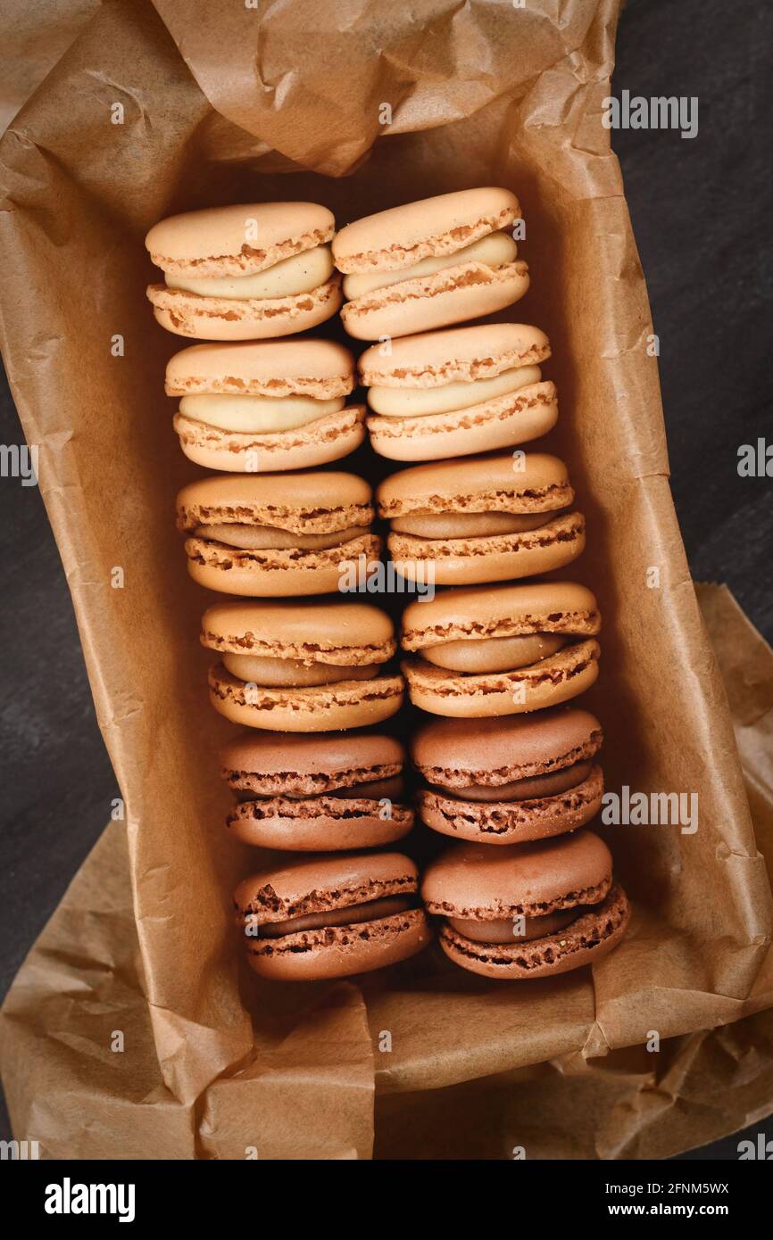 Macaron francesi di colore marrone, beige e crema con aroma di caffè, moka, cioccolato e vaniglia in teglia con carta da forno Foto Stock