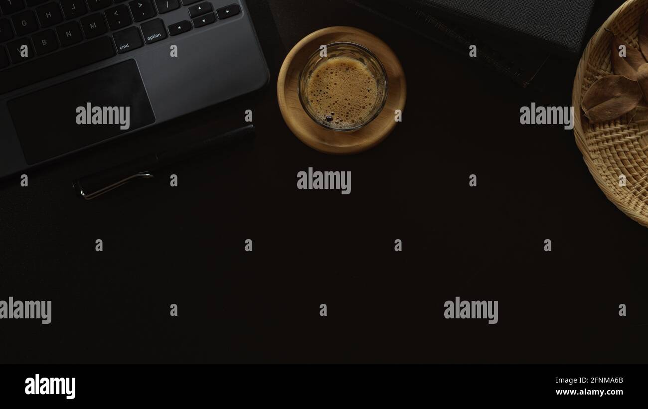 Vista dall'alto dell'area di lavoro con tazza da caffè, tastiera e spazio per la copia su un tavolo nero Foto Stock