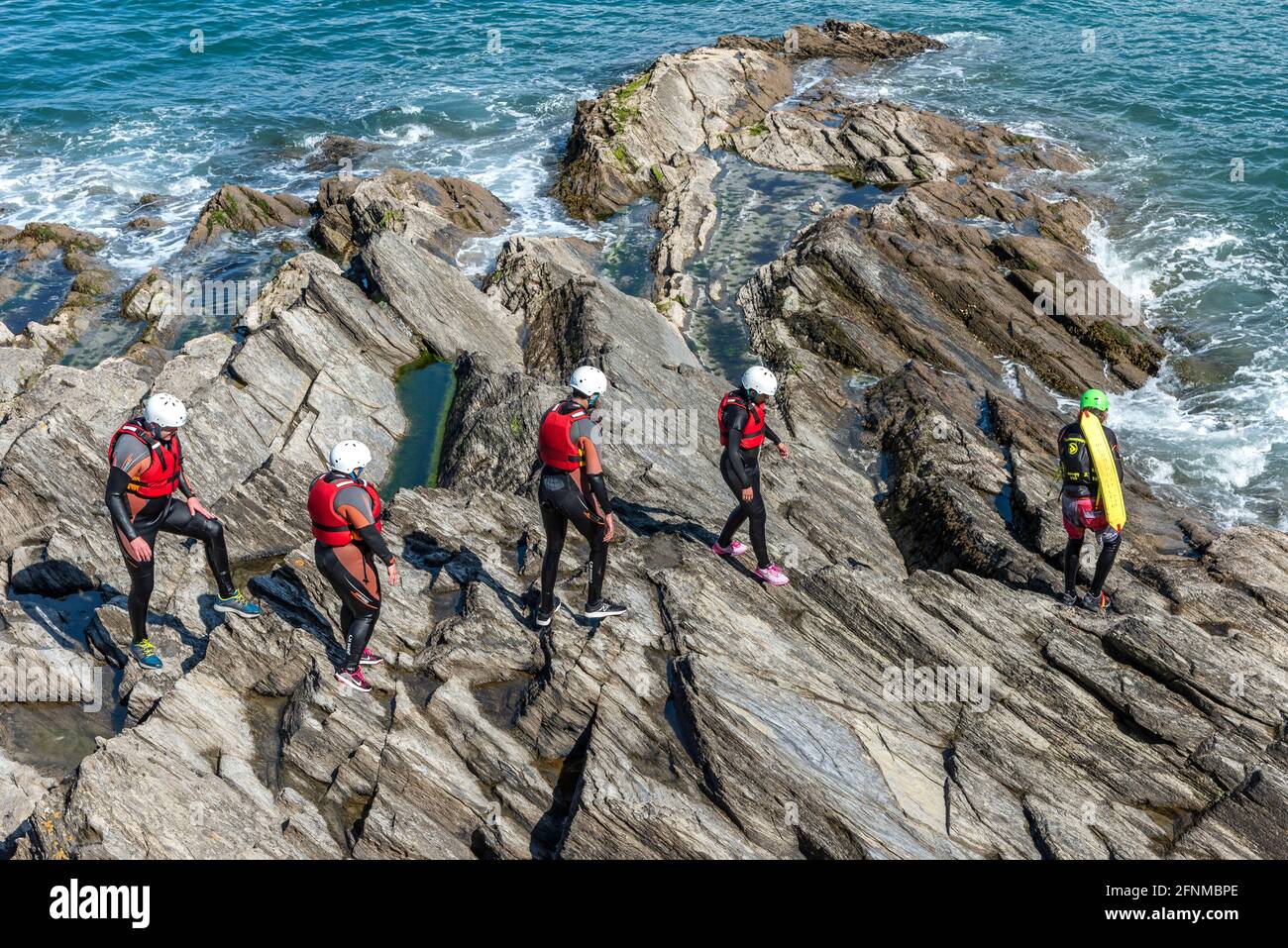 I turisti che camminano attraverso le rocce seguendo la loro guida coastering sulla costa di Towan Head a Newquay in Cornovaglia. Foto Stock