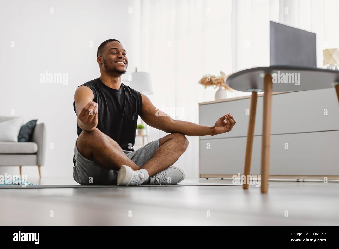 Black Man meditando al laptop seduto in posizione Lotus Indoor Foto Stock