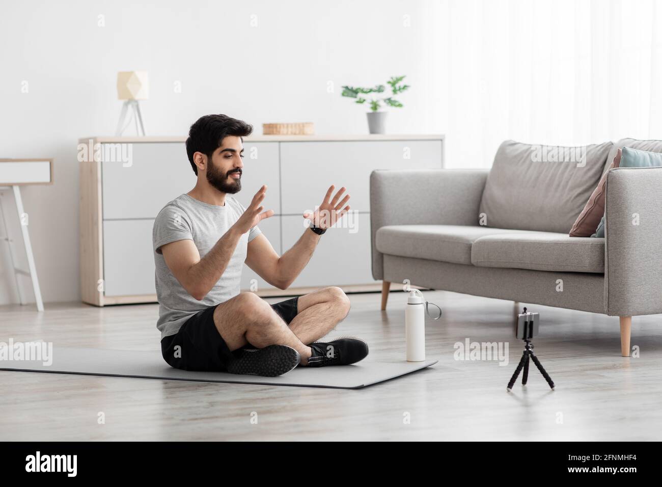Amichevole giovane uomo arabo bearded registra sugli sport della webcam del telefono blog in soggiorno Foto Stock