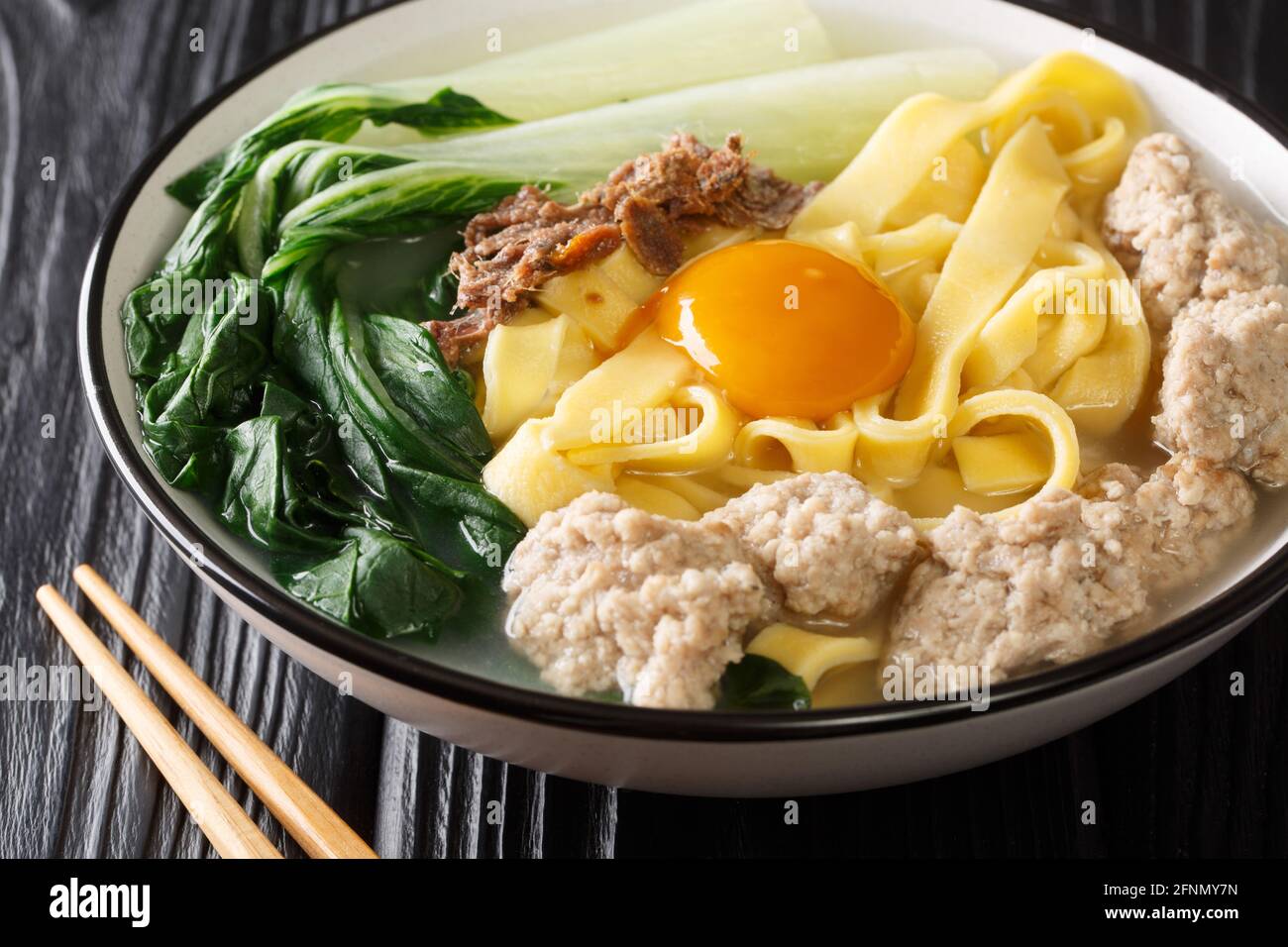 Ban Mian zuppa cinese di noodle uovo con acciughe, polpette e pak choi primo piano in una ciotola sul tavolo. Orizzontale Foto Stock