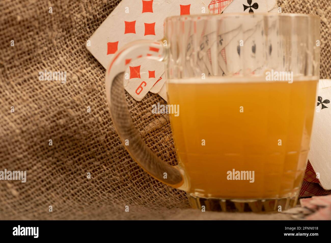 Carte da gioco e una tazza di birra leggera non filtrata su un tavolo coperto di stoffa grossolana. Primo piano, messa a fuoco selettiva. Foto Stock