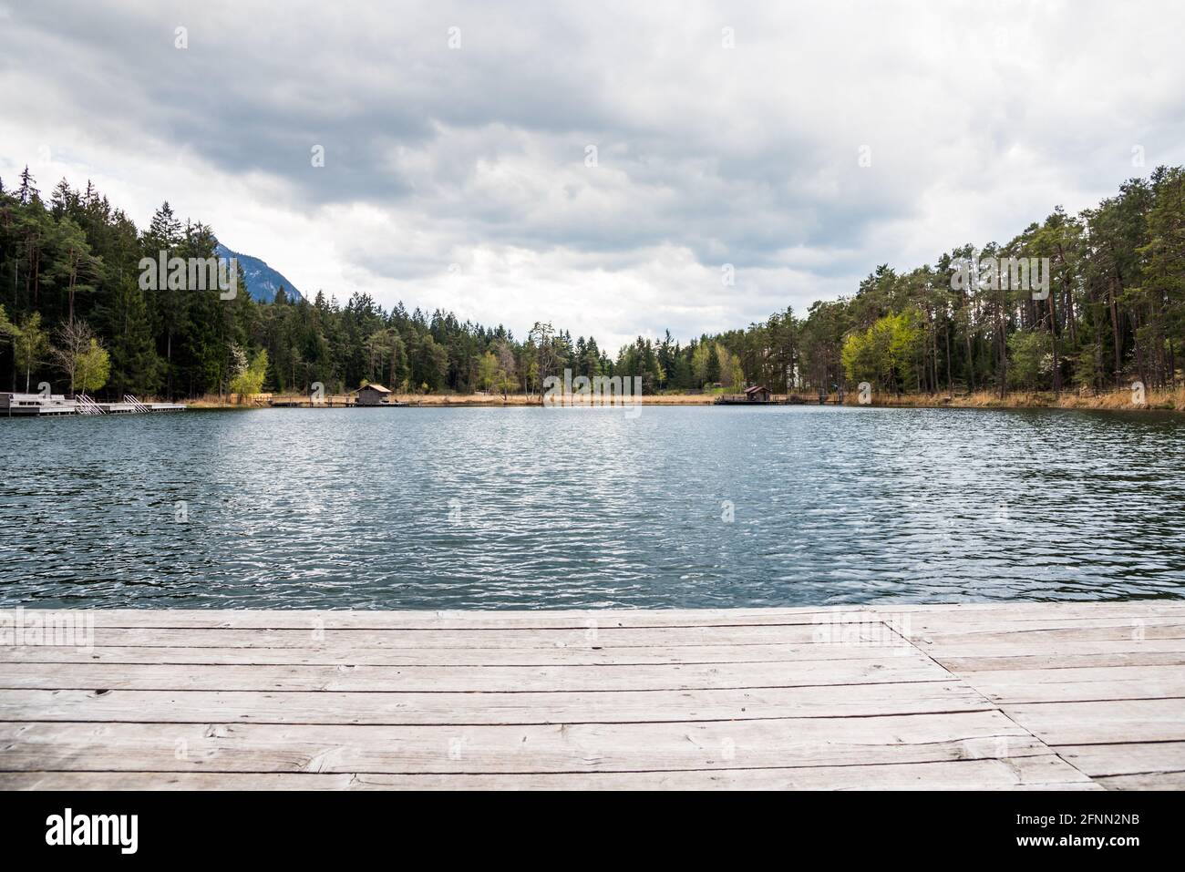 Piattaforma in legno su un piccolo lago di montagna nelle Alpi il giorno tempestoso di primavera Foto Stock
